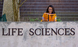 Cindy Nguyen reading a book in front of the Life Sciences building at LSU