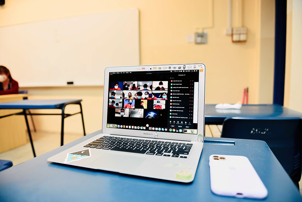 laptop sitting on a desk in a classroom with a Zoom meeting on the screen