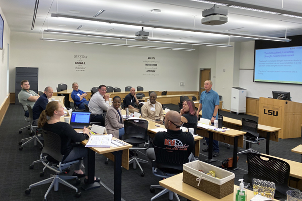 Students in a classroom looking at an instuctor that is standing and speaking. 