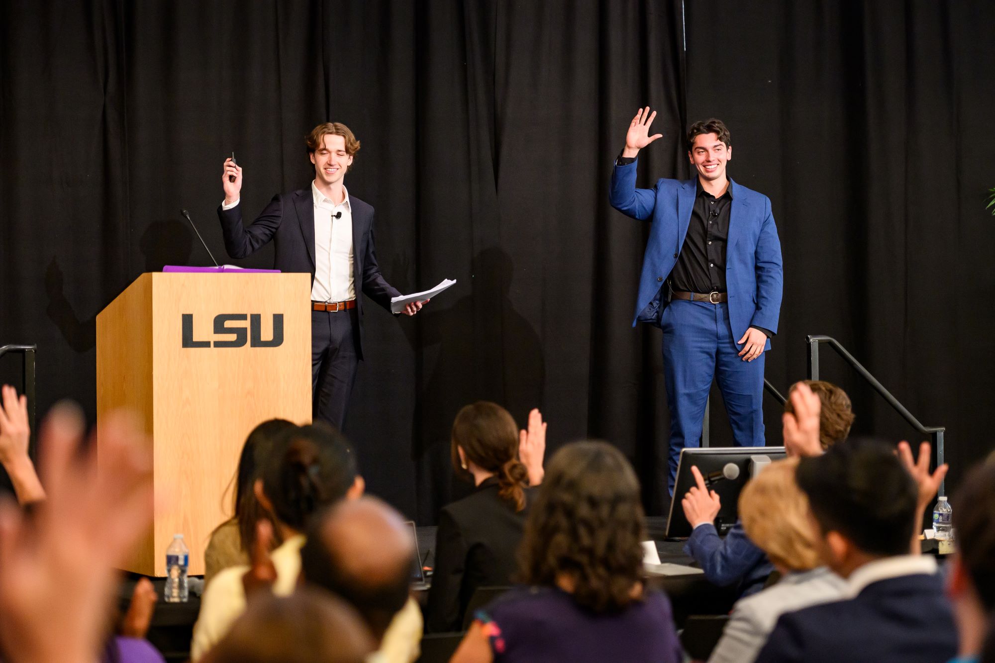 Two students on a stage with their hands raised